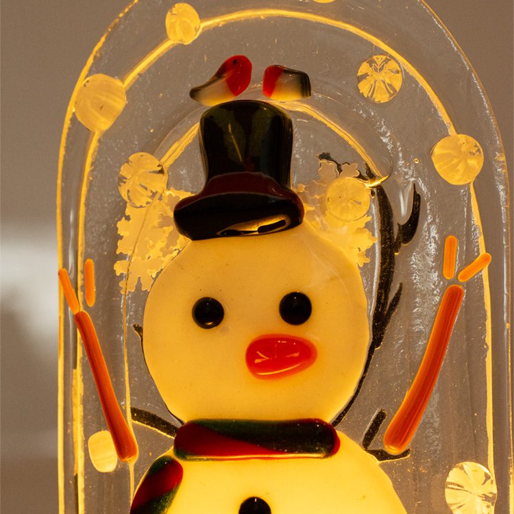 Close-up of illuminated fused glass snowglobe snowman wearing black top hat