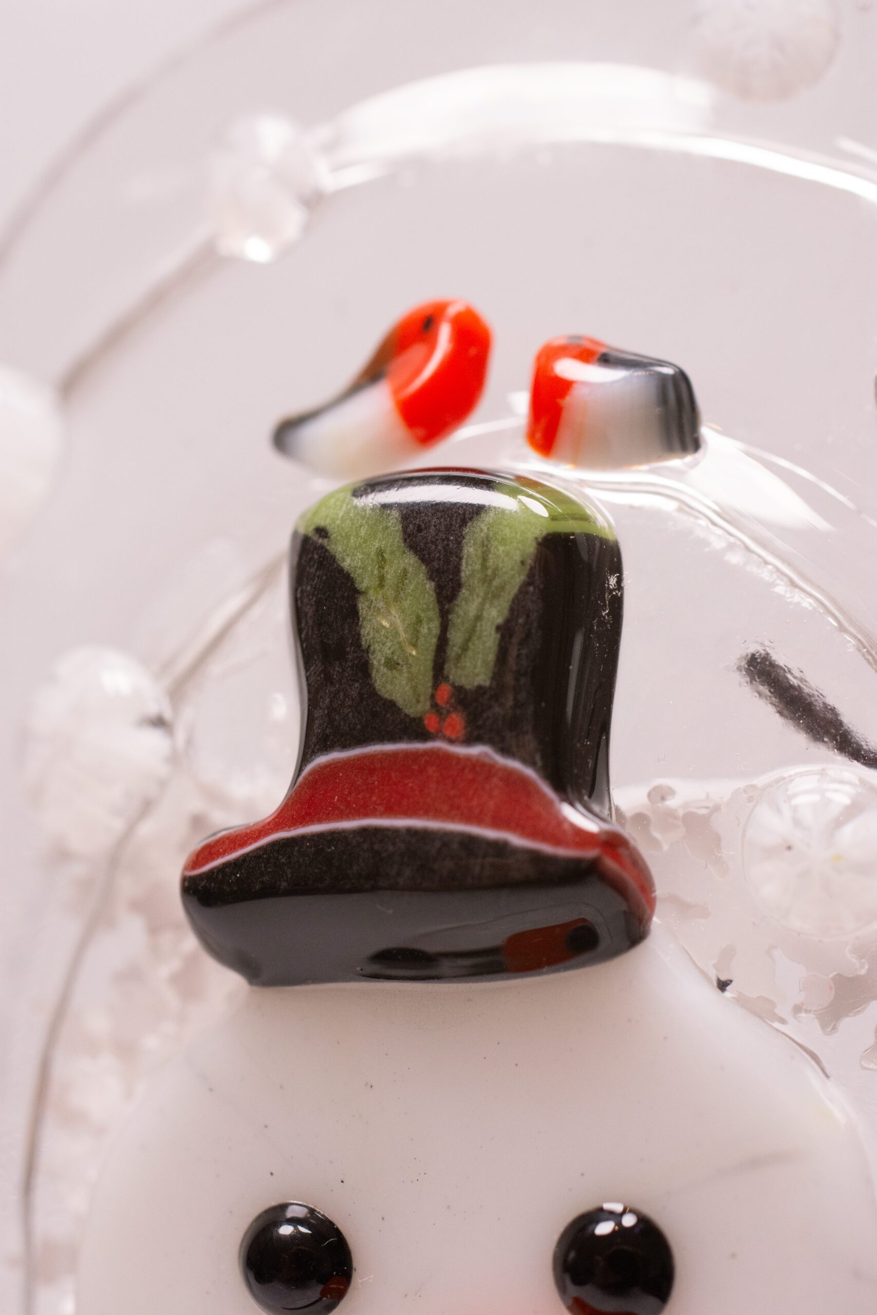Close-up of black top hat with holly on fused glass snowman